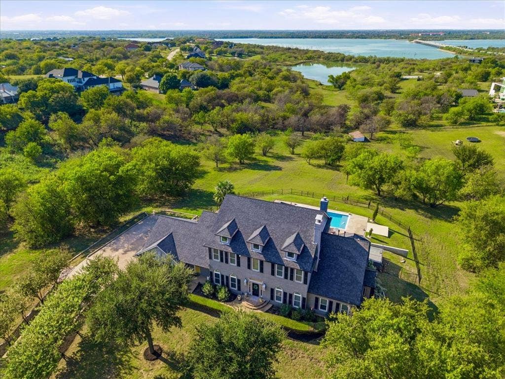 2945 Emerald Sound Drive, Cedar Hill, TX 75104 Multi-story residence featuring a shingled roof, dormer windows, shuttered exterior detailing, and a backyard swimming pool set on a sprawling parcel with mature trees