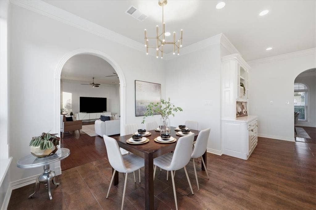 2945 Emerald Sound Drive, Cedar Hill, TX 75104 Dining space featuring arched entryways, wood-finish flooring, built-in cabinetry, crown molding, and a modern multi-arm chandelier