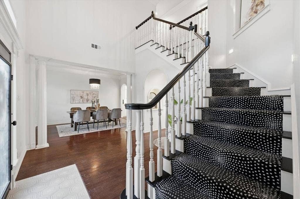 2945 Emerald Sound Drive, Cedar Hill, TX 75104 Foyer featuring double-height ceilings, wood-finish flooring, and a staircase with white balusters, a dark handrail, and patterned carpet runner