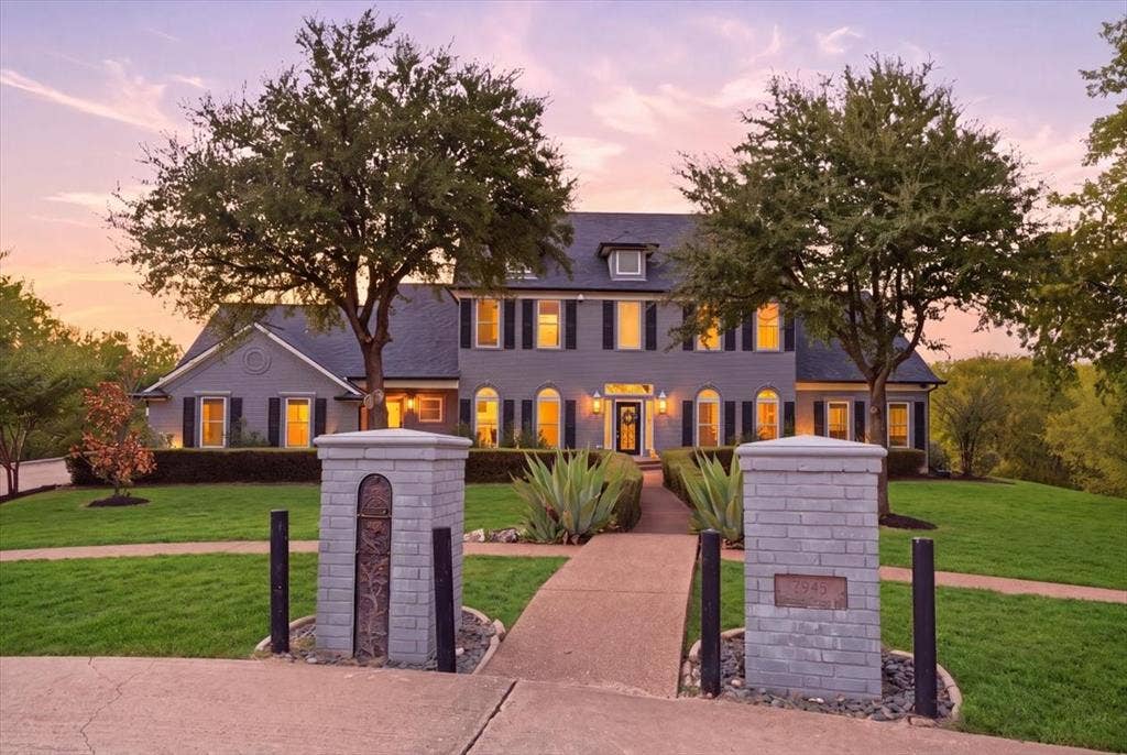 2945 Emerald Sound Drive, Cedar Hill, TX 75104 Two-story residence featuring a gray siding exterior, dark shutters, gabled rooflines, decorative brick entry pillars, and mature landscaping