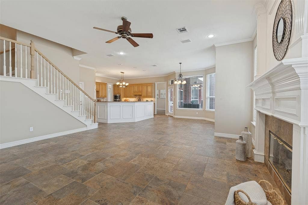 2704 Horsehead Crossing, Southlake, TX 76092 Open-concept interior featuring large-format stone tile flooring, a fireplace with a white millwork mantel, wooden staircase with white balusters, and a kitchen island with white cabinetry