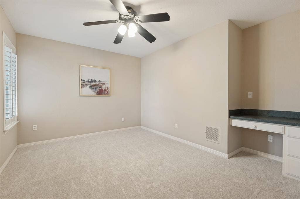 2704 Horsehead Crossing, Southlake, TX 76092 Carpeted interior space featuring a ceiling fan with integrated lighting, plantation shutters, and a built-in desk with stone-finish countertop and cabinetry