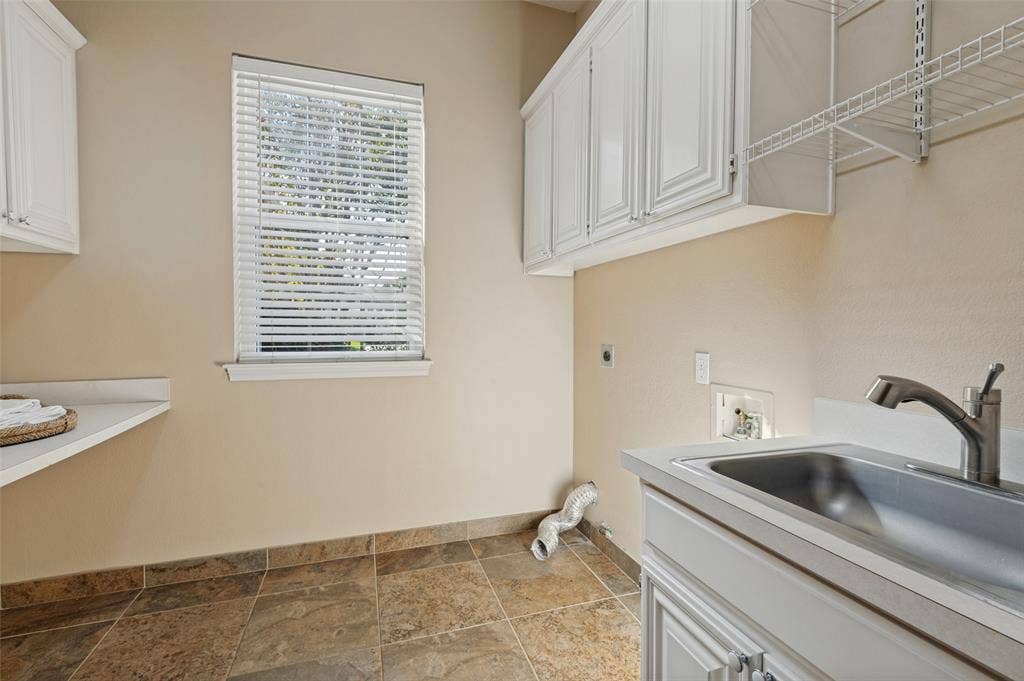 2704 Horsehead Crossing, Southlake, TX 76092 Laundry space featuring white shaker-style cabinetry, a stainless steel utility sink with a chrome faucet, stone-finish tile flooring, and a fixed laminate countertop