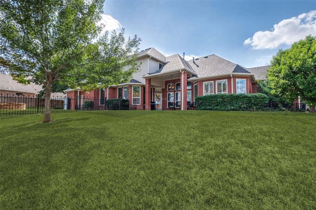 2704 Horsehead Crossing, Southlake, TX 76092 Expansive backyard featuring a manicured lawn, mature trees, metal perimeter fencing, brick-and-siding exterior, and a covered patio