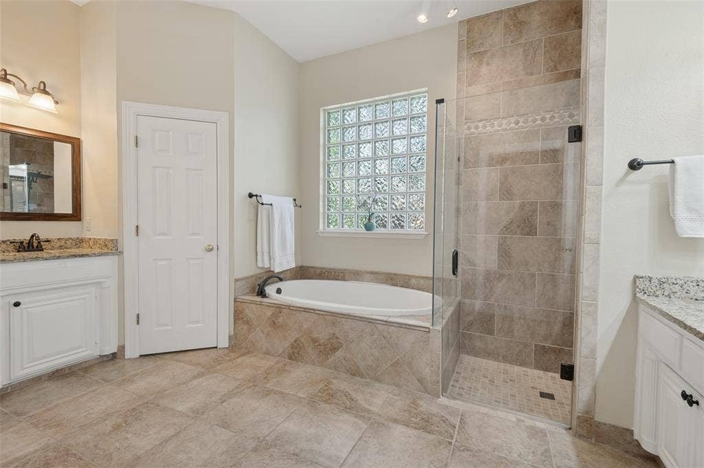 2704 Horsehead Crossing, Southlake, TX 76092 Dual vanity area featuring stone-look countertops, soaking tub with tile surround, glass-enclosed walk-in shower, and glass block window