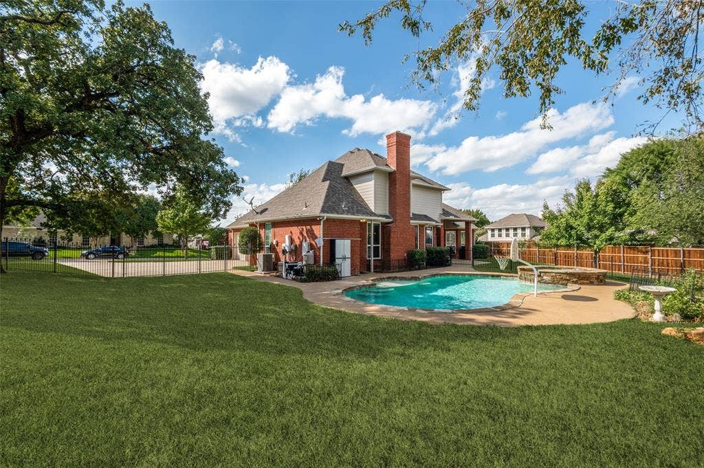 2704 Horsehead Crossing, Southlake, TX 76092 Rear exterior featuring a brick and siding facade, an expansive lawn, a built-in swimming pool with an attached spa, and a concrete patio