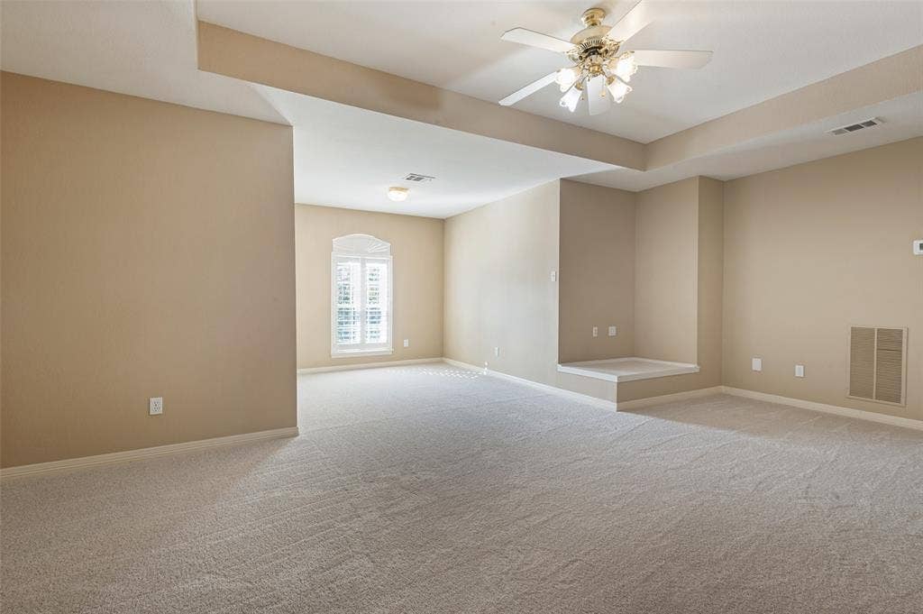 2704 Horsehead Crossing, Southlake, TX 76092 Spacious room featuring a tray ceiling, neutral wall-to-wall carpeting, an arched window with plantation shutters, a built-in architectural alcove, and a multi-blade ceiling fan with integrated lighting