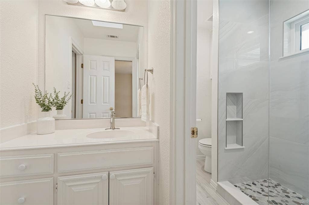 2704 Horsehead Crossing, Southlake, TX 76092 Bathroom vanity with a white countertop and oval under-mount sink, large wall-mounted mirror, walk-in shower with tile surround, built-in shower niche, and stone-tiled shower floor