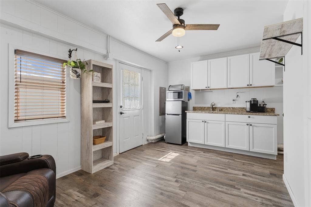 Wood-finish flooring, white paneling, ceiling fan, white cabinetry, and a granite-style countertop