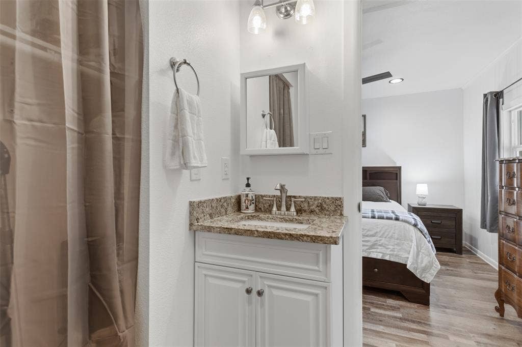 Bathroom vanity with granite-style countertop, white cabinetry, and brushed nickel faucet