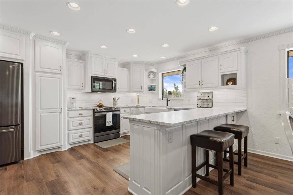 White shaker cabinetry, stainless steel appliances, wood-finish flooring, recessed lighting, and a white subway tile backsplash