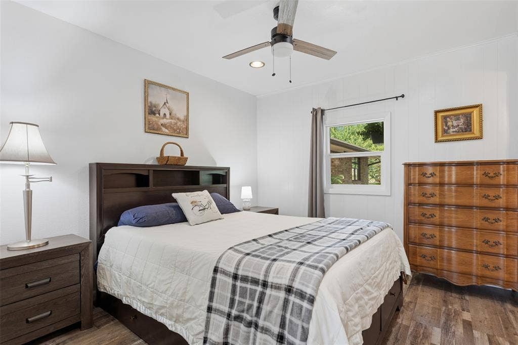 Wood-finish flooring, ceiling fan with light fixture, window with drapes, and paneled accent wall