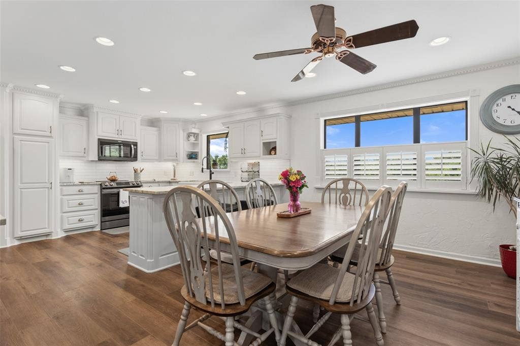 Kitchen and dining area featuring wood-finish flooring, white cabinetry, a kitchen island with seating, a window with plantation shutters, and recessed lighting