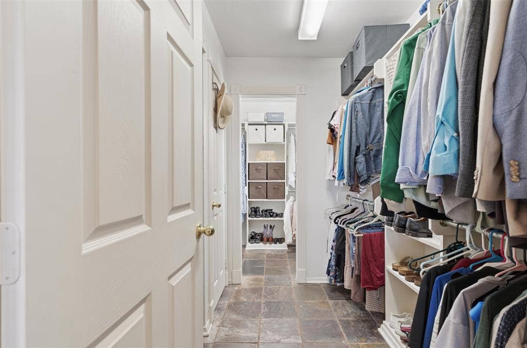 Walk-in closet featuring stone tile flooring, built-in shelving, and multiple hanging rods