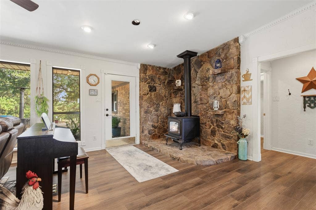 Wood-finish flooring, recessed lighting, crown molding, stone-clad accent wall, and a built-in wood-burning stove