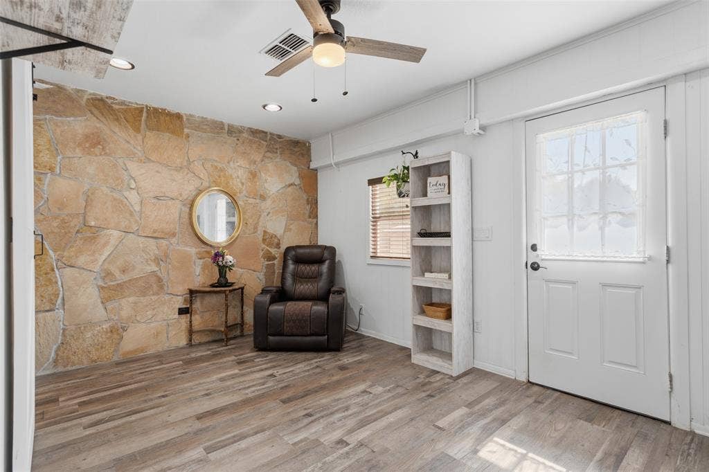 Stone accent wall, wood-finish flooring, recessed lighting, ceiling fan, and a paneled entry door with frosted glass