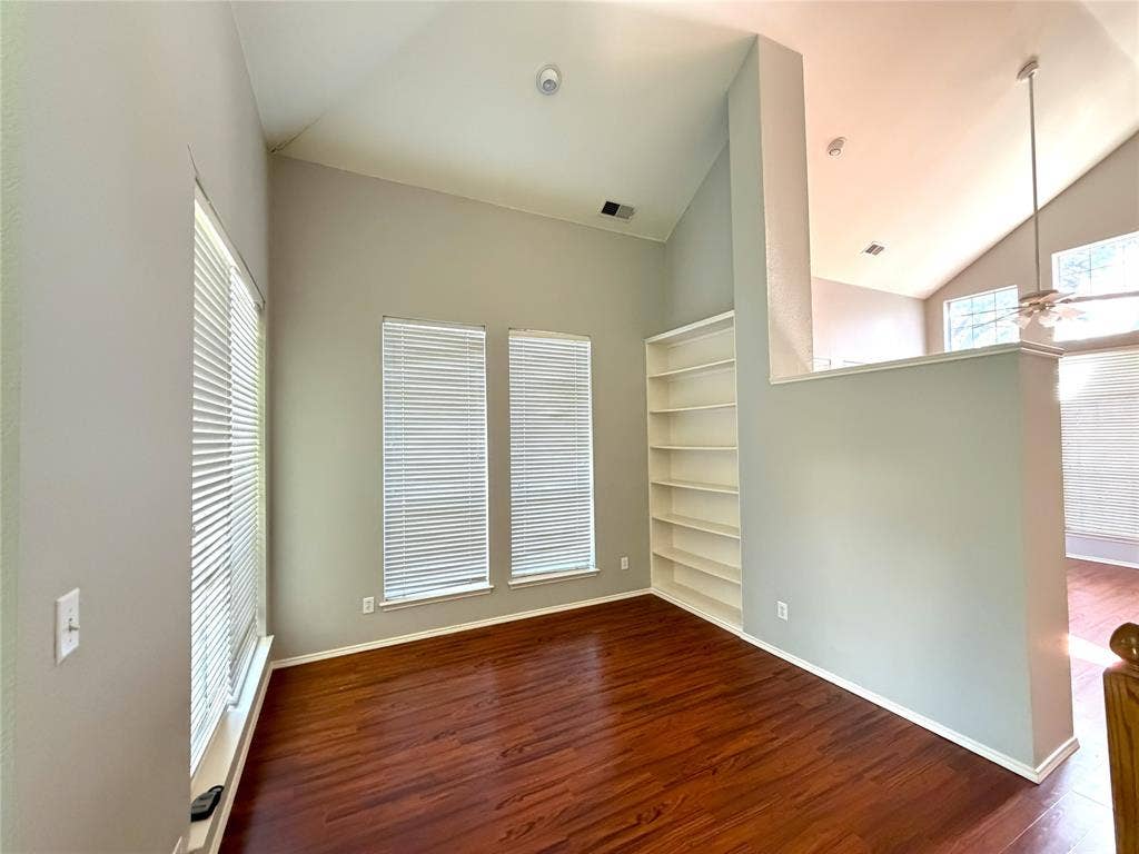Wood-finish flooring, built-in shelving, vaulted ceilings, and multiple windows with blinds
