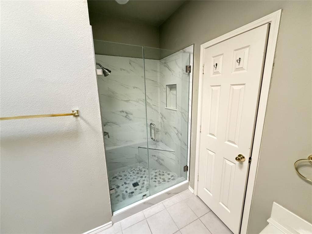 Glass-enclosed shower with a built-in niche, pebble-style shower floor, and large format wall tile