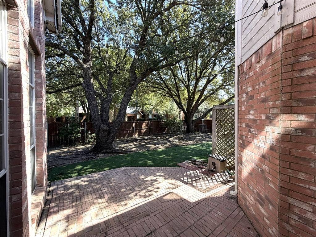 Brick paver patio with a lattice screen, artificial turf, and mature shade trees