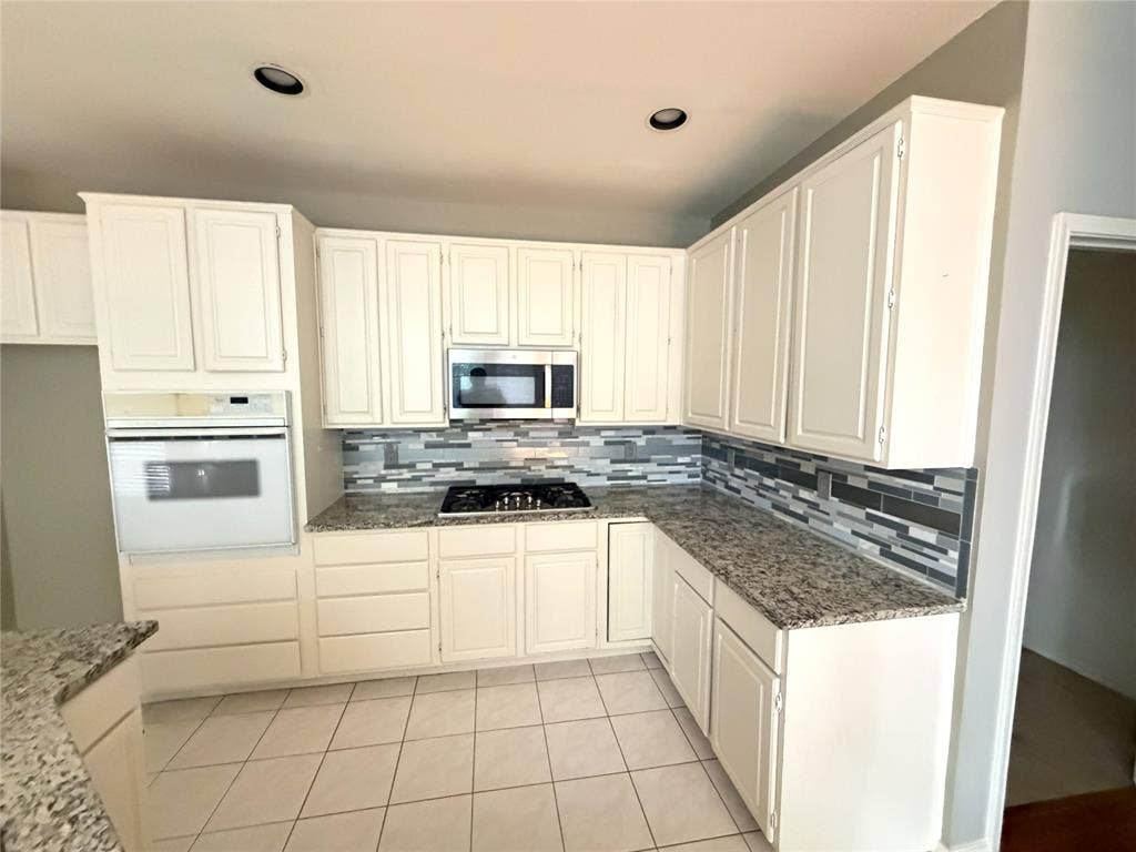 Recessed lighting, extensive white cabinetry, granite-finish countertops, tiled backsplash, and tile flooring