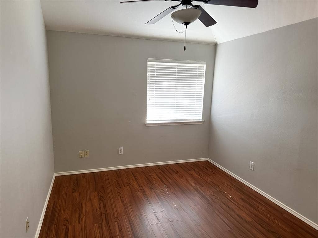 Wood-finish flooring with white trim, a window with blinds, and a ceiling fan with integrated lighting