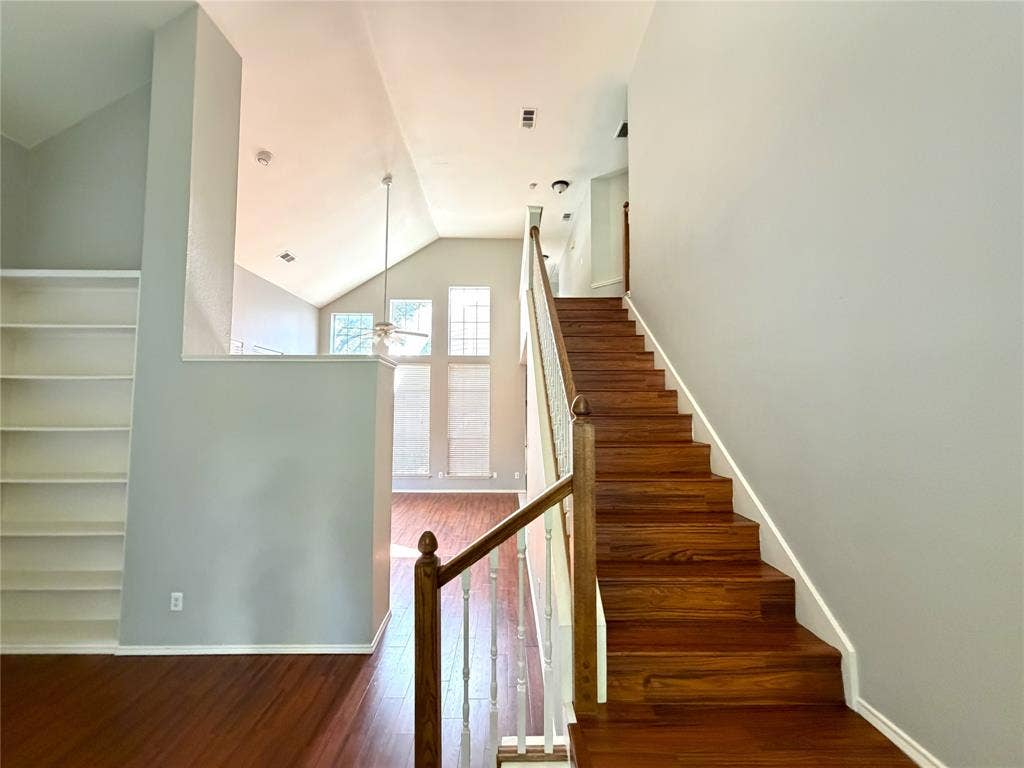 Vaulted ceiling, built-in shelving, wood-finish flooring, staircase with wood-finish treads, and large windows