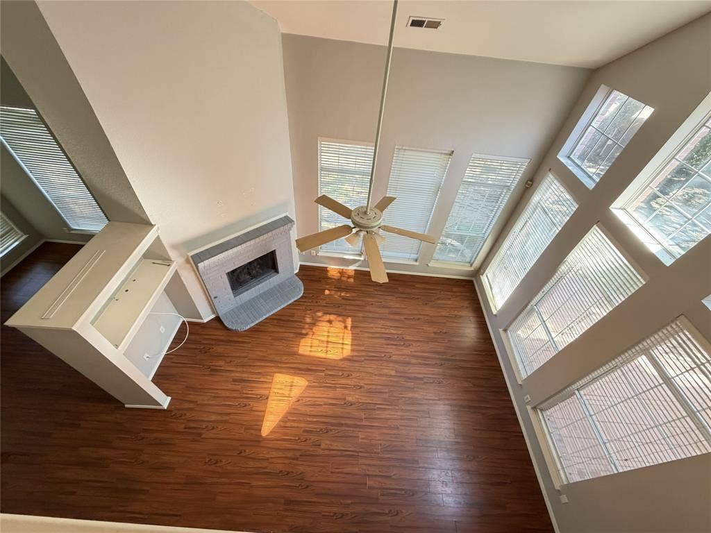 Vaulted ceiling featuring a ceiling fan, a fireplace with a hearth, wood-finish flooring, built-in shelving, and multiple windows with blinds