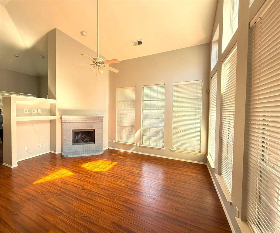 Vaulted ceiling, wood-finish flooring, brick fireplace, built-in shelving, and large windows
