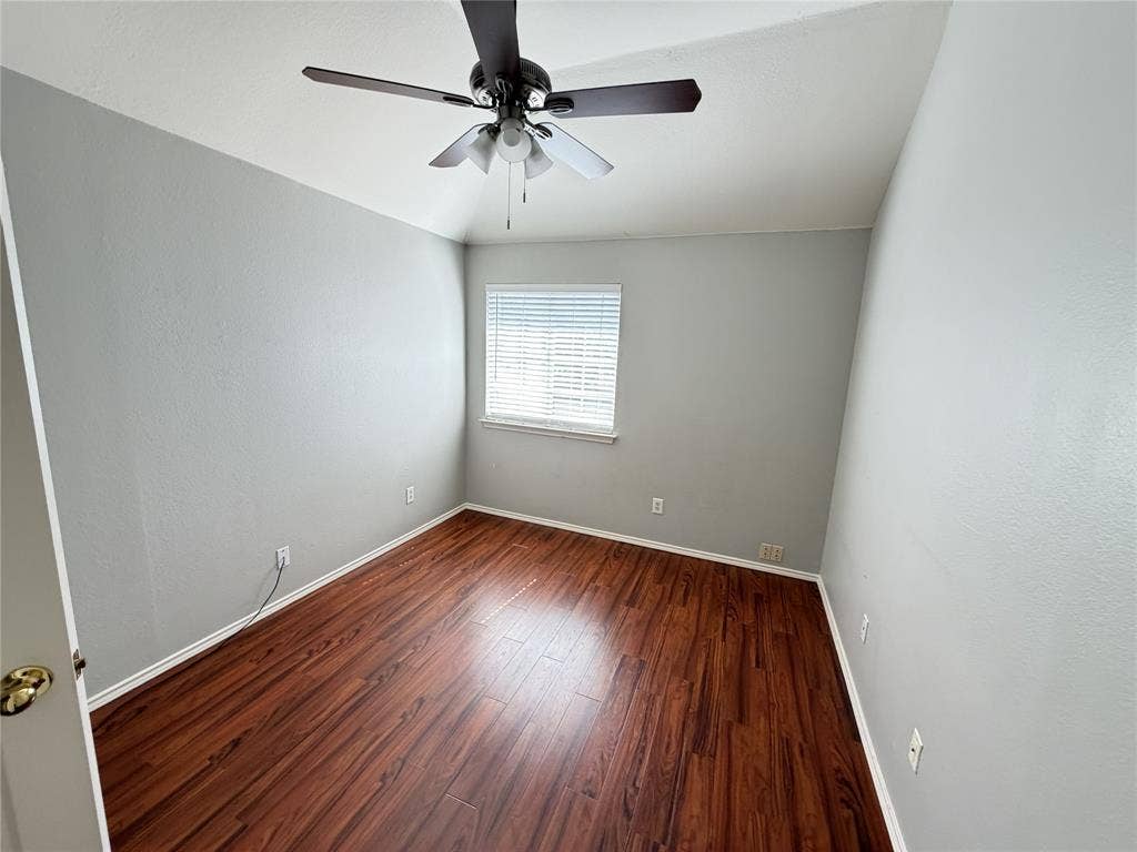 Wood-finish flooring, ceiling fan, window with blinds, and light gray wall finish
