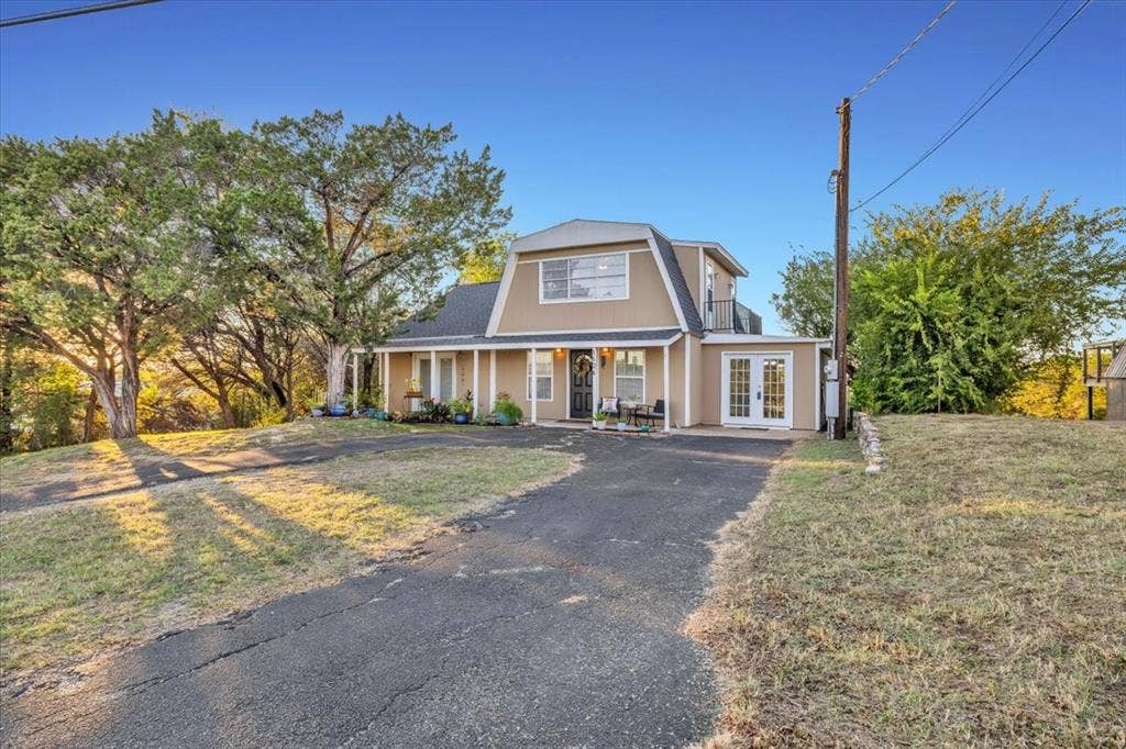 1106 Scenic Drive, Granbury, TX 76048 Gambrel-style residence featuring a covered front porch, dual-entry French doors, and a paved driveway