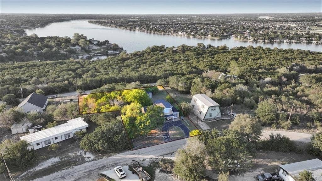 1106 Scenic Drive, Granbury, TX 76048 Aerial perspective of a property featuring mature trees, paved driveway, and proximity to a large body of water