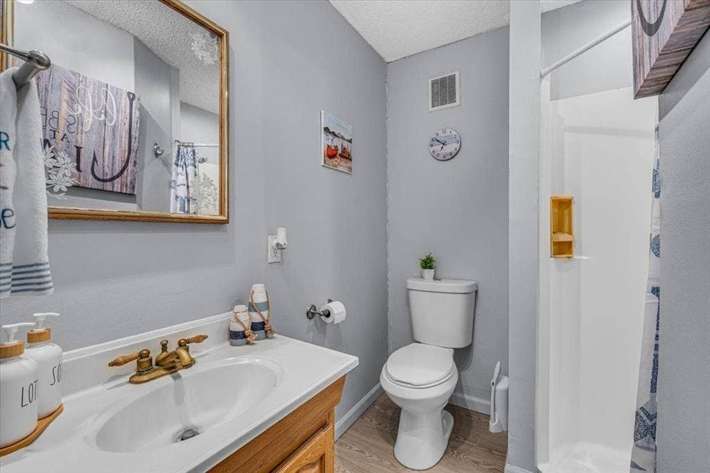 1106 Scenic Drive, Granbury, TX 76048 Bathroom featuring a wood-finish vanity with an integrated white sink, metallic faucet hardware, wood-finish flooring, and a walk-in shower surround