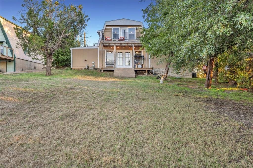 1106 Scenic Drive, Granbury, TX 76048 Rear exterior featuring a covered deck, second-story balcony with metal railings, French doors, and mature landscaping