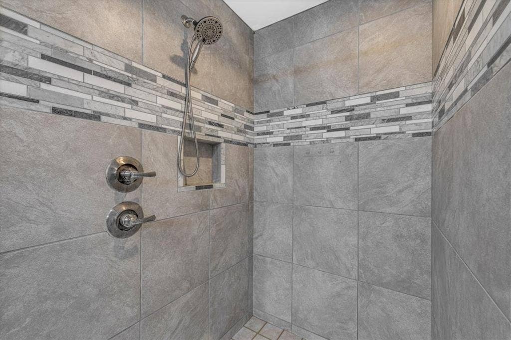 1106 Scenic Drive, Granbury, TX 76048 Walk-in shower featuring large-format grey tile, a decorative linear mosaic accent border, a built-in tiled niche, and chrome rainfall shower head with dual-handle controls