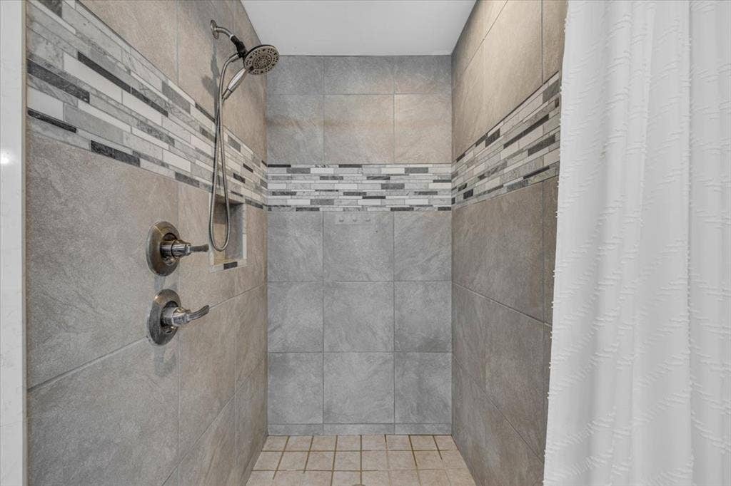 1106 Scenic Drive, Granbury, TX 76048 Shower stall featuring large-format grey wall tile, a horizontal mosaic tile accent border, a built-in recessed soap niche, and a wall-mounted shower head with adjustable handheld attachment