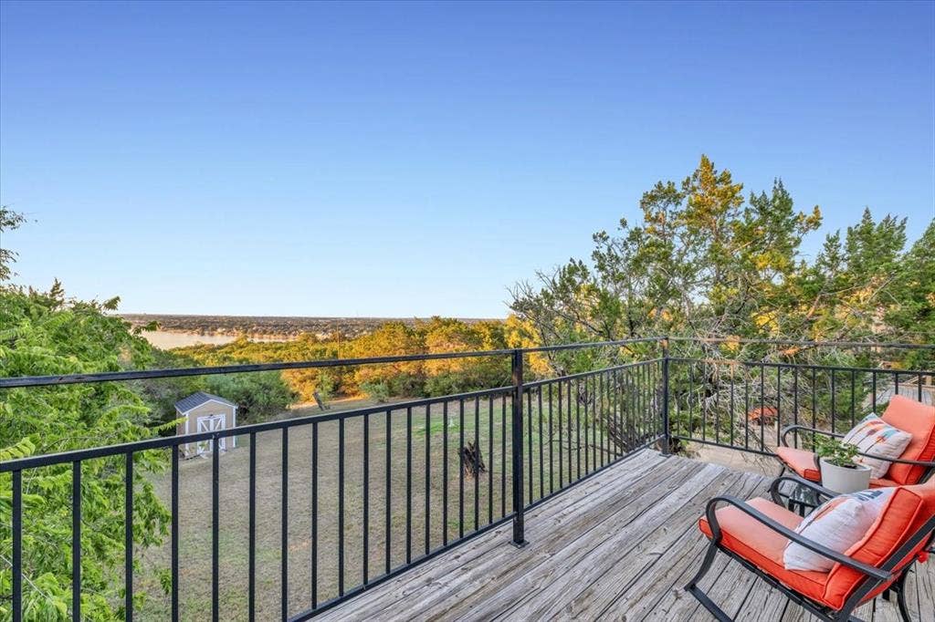 1106 Scenic Drive, Granbury, TX 76048 Elevated wooden deck with black metal railing overlooking a landscape featuring mature trees and a detached storage shed