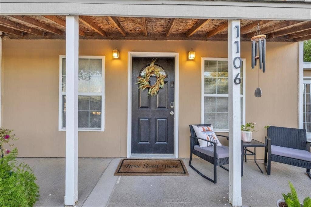 1106 Scenic Drive, Granbury, TX 76048 Covered front porch featuring a concrete foundation, dual exterior wall-mounted sconces, and a paneled entry door with an arched glass inset