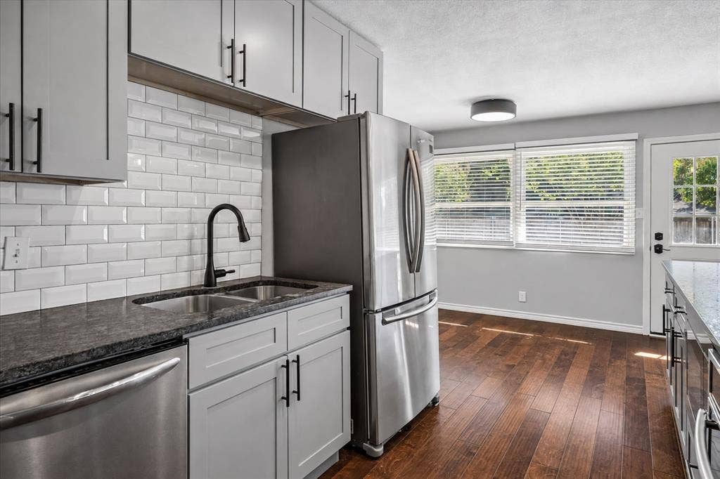 Kitchen featuring light gray cabinetry, stainless steel appliances, dark stone-finish countertops, and wood-finish flooring