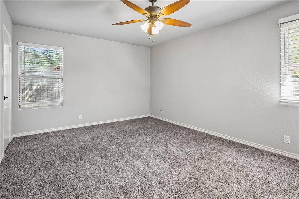 Room featuring gray textured carpeting, neutral wall paint, and two windows with blinds