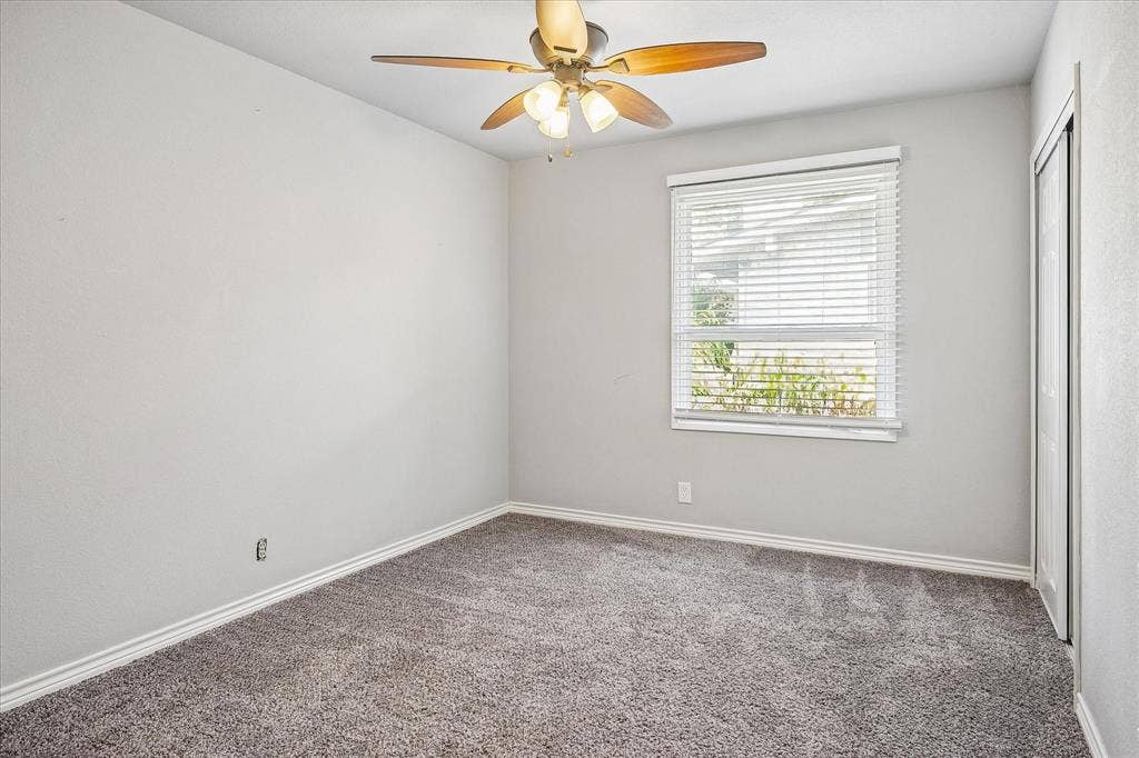 Neutral wall paint, plush carpet flooring, window with blinds, ceiling fan with light fixture, and closet with sliding doors