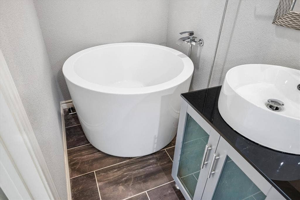 Freestanding soaking tub, vessel sink, vanity with frosted glass doors, dark countertop, and tile flooring