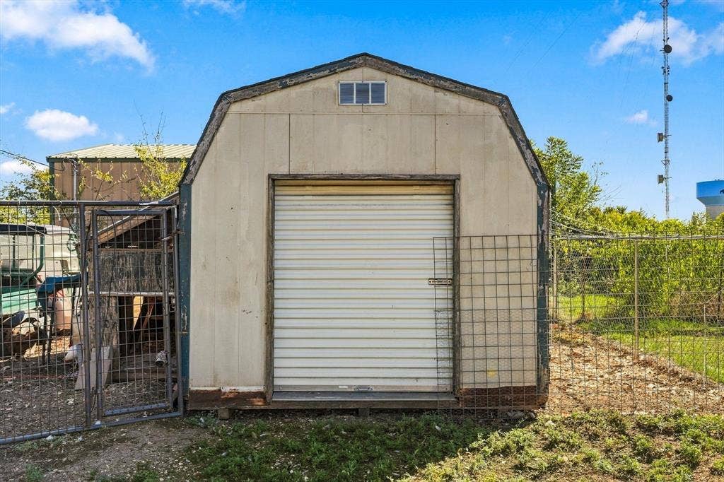 1320 Apple Lane, Midlothian, TX 76065 12 x 10 Outbuilding featuring a gambrel roof design, a roll-up metal door, and exterior metal wire fencing
