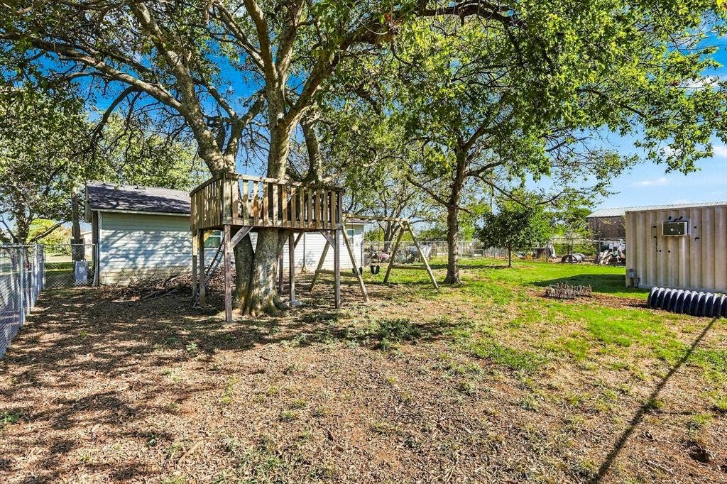 1320 Apple Lane, Midlothian, TX 76065 Backyard area featuring mature hardwood trees, a wood-frame tree house and playground, and chain link perimeter fencing