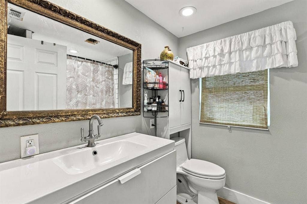 1320 Apple Lane, Midlothian, TX 76065 Modern vanity with integrated basin and polished metal faucet, large wall-mounted ornate gold-tone framed mirror, recessed lighting, and built-in vertical storage cabinet
