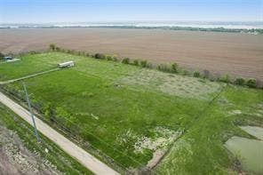Lot 3 Bozek Lane, Ennis, TX 75119 Expansive agricultural land featuring a verdant field, unpaved access road, and water feature