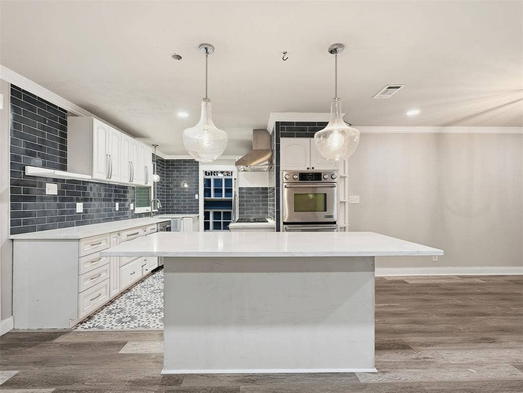 1402 Addington Street, Irving, TX 75062 Contemporary kitchen featuring white cabinetry, a large center island with a light-toned countertop, and stainless steel built-in appliances