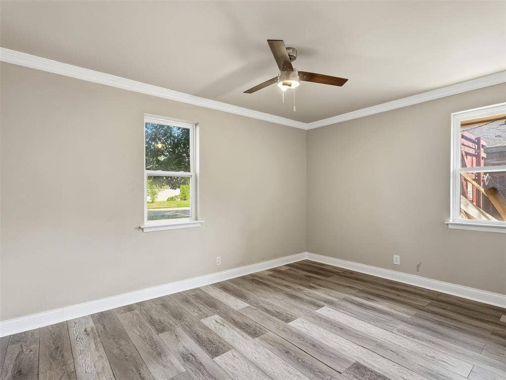 1402 Addington Street, Irving, TX 75062 Wood-finish flooring, neutral wall tones, two windows with white trim, white crown molding, and a ceiling fan with light fixture