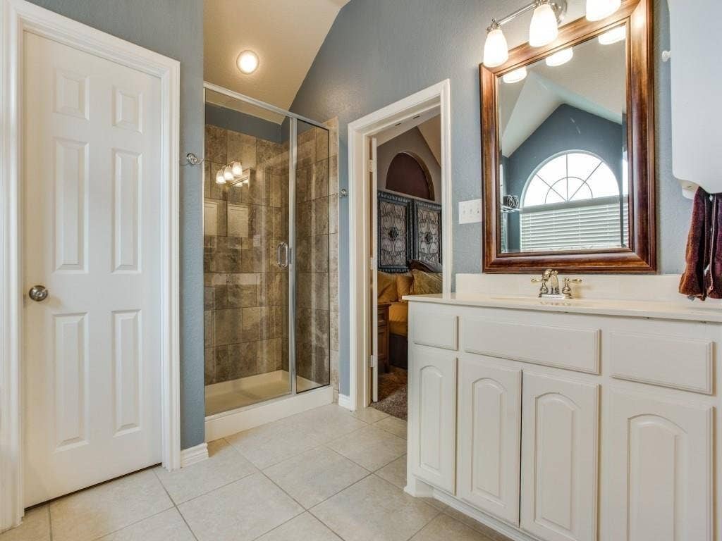 12316 Sailmaker Lane, Frisco, TX 75035 White single vanity with a laminate countertop, a framed mirror, a glass-enclosed shower, and tile flooring