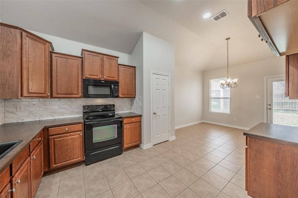 2205 Clairborne Drive, Fort Worth, TX 76177 Kitchen featuring wood cabinetry, dark countertops, black appliances, and a tiled backsplash