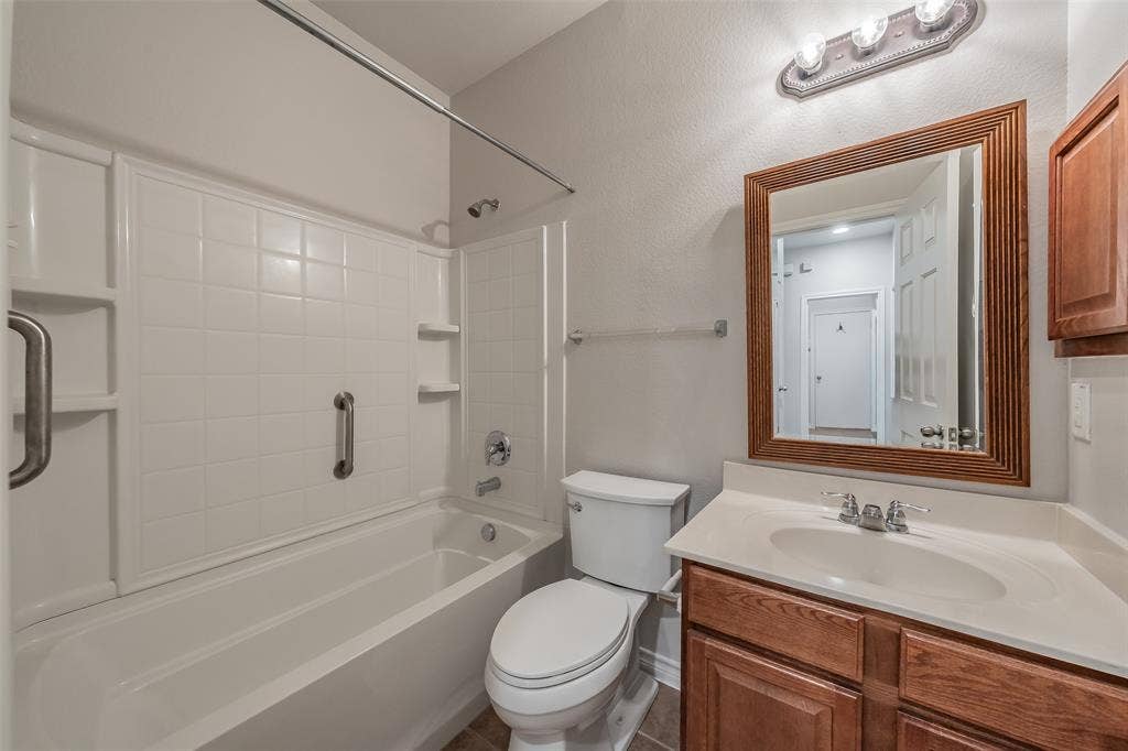 2205 Clairborne Drive, Fort Worth, TX 76177 Built-in bathtub with white tile surround, wood-finish vanity with countertop, framed mirror, and chrome fixtures